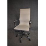 A Charles Eames style swivel office armchair in cream vinyl upholstery. H.114x50cm