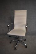 A Charles Eames style swivel office armchair in cream vinyl upholstery. H.114x50cm