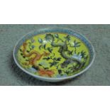 A Chinese yellow ground hand painted porcelain dish depicting two dragons, one red and one black.