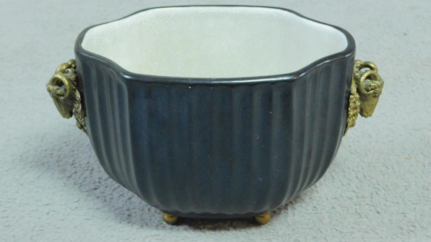 A Black antique style ribbed porcelain planter with two brass buck heads and mounted on brass