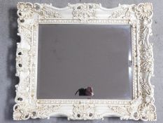 A white lacquered floral scrolling framed wall mirror fitted with bevelled plate. 68x58cm
