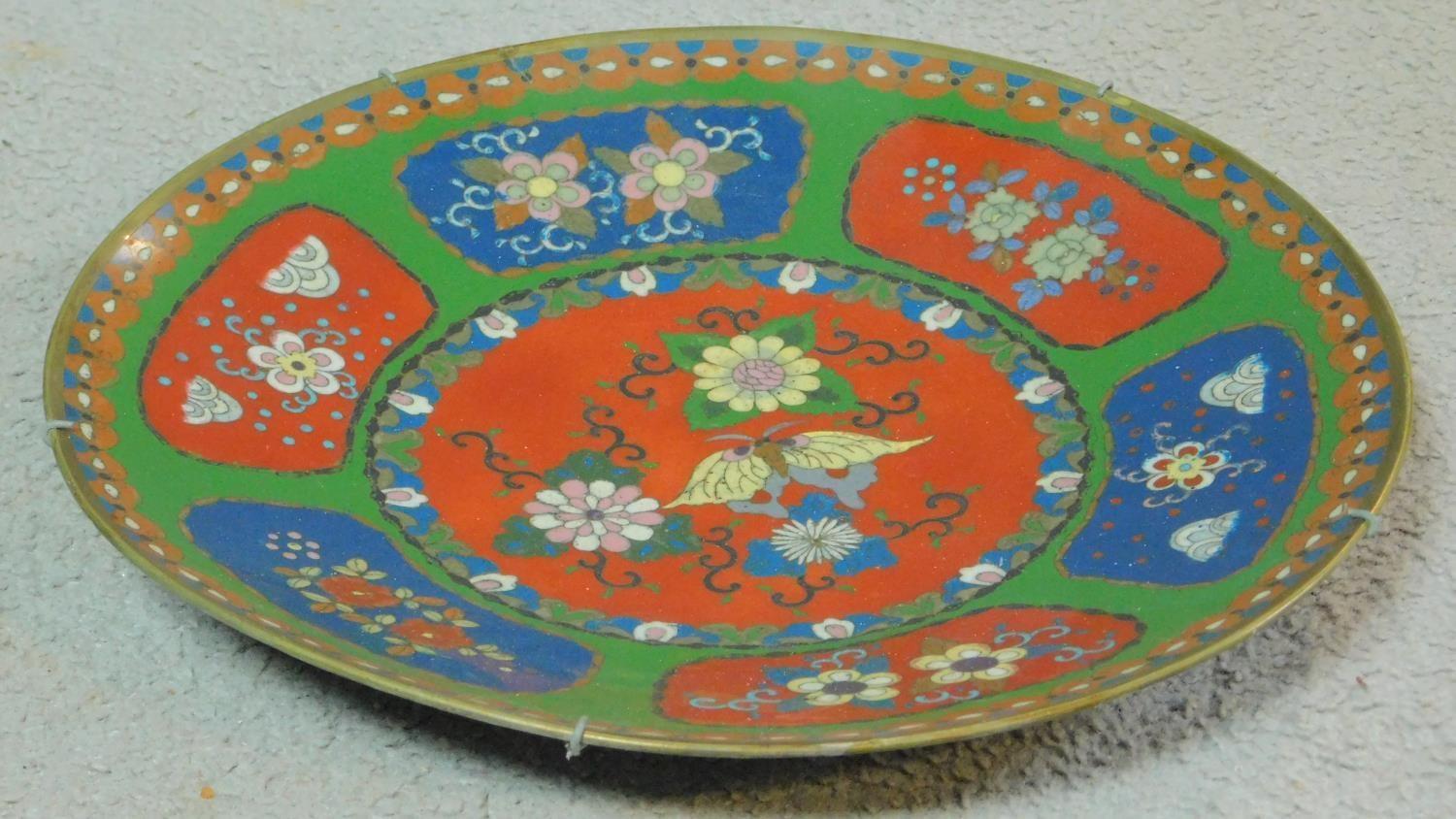 A Meji period Cloisonné enamel plate with red and blue panels on a green background decorated with