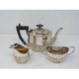 A matched three piece dragooned silver tea set. The ebony handled tea pot hallmarked: WA for William