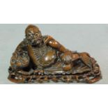A 20th century carved Chinese hardwood lying deity on pierced base. Glass eyes for the man and lion.