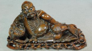 A 20th century carved Chinese hardwood lying deity on pierced base. Glass eyes for the man and lion.