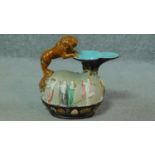 An antique Majolica hand painted glazed pitcher with a leaping lion handle standing on a sculpted