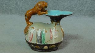 An antique Majolica hand painted glazed pitcher with a leaping lion handle standing on a sculpted