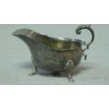 A sterling silver sauce boat with stylised foliate handle sitting on three hooved feet and with