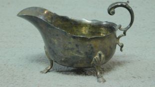 A sterling silver sauce boat with stylised foliate handle sitting on three hooved feet and with