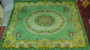 A large woollen carpet with central oval floral medallion on sage ground within floral border.