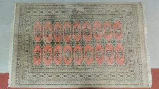 A woollen Bokhara style carpet with repeating lozenge motifs on rouge ground contained within
