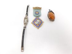 An Art Deco silver and diamante ladies watch with a silver enamel masonic medal and an amber brooch.