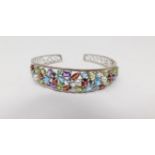 A multi gemstone and silver scrolling design pierced bangle. Set with forty eight mixed cut