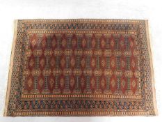 A Bokhara style rug with repeating lozenge motifs on a burgundy ground contained in a geometric