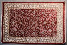 A Persian hand tufted silk rug with repeating floral motifs on burgundy ground within foliate