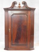 A Georgian mahogany corner cupboard with broken swan neck pediment above fielded panel door