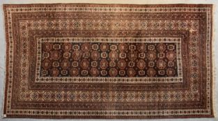 A Turkoman carpet with repeating gul moifs on a chocolate ground contained within stylised floral
