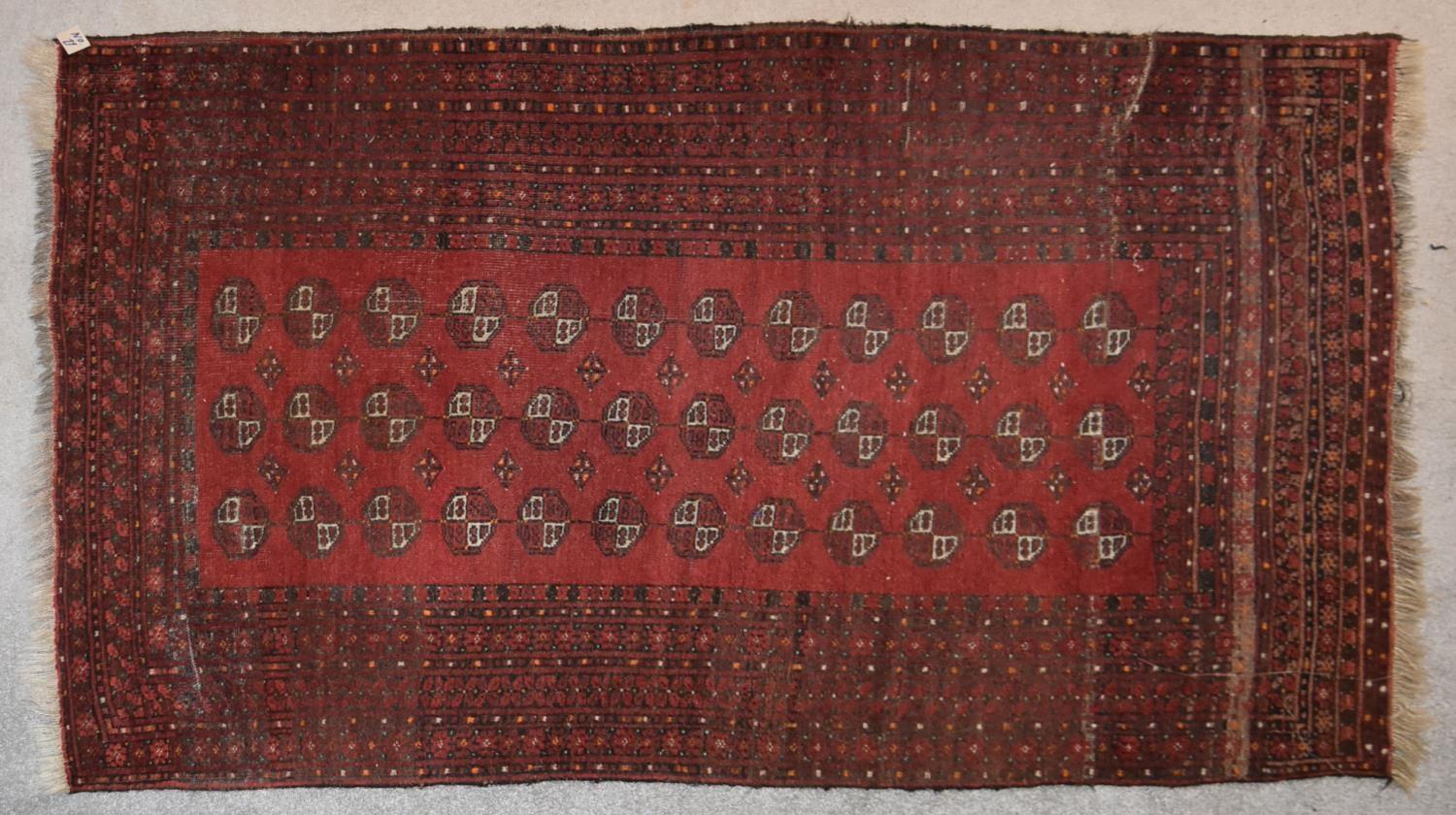 An Afghan Bokhara rug with repeating elephant's pad motifs on crimson ground within stylised multi