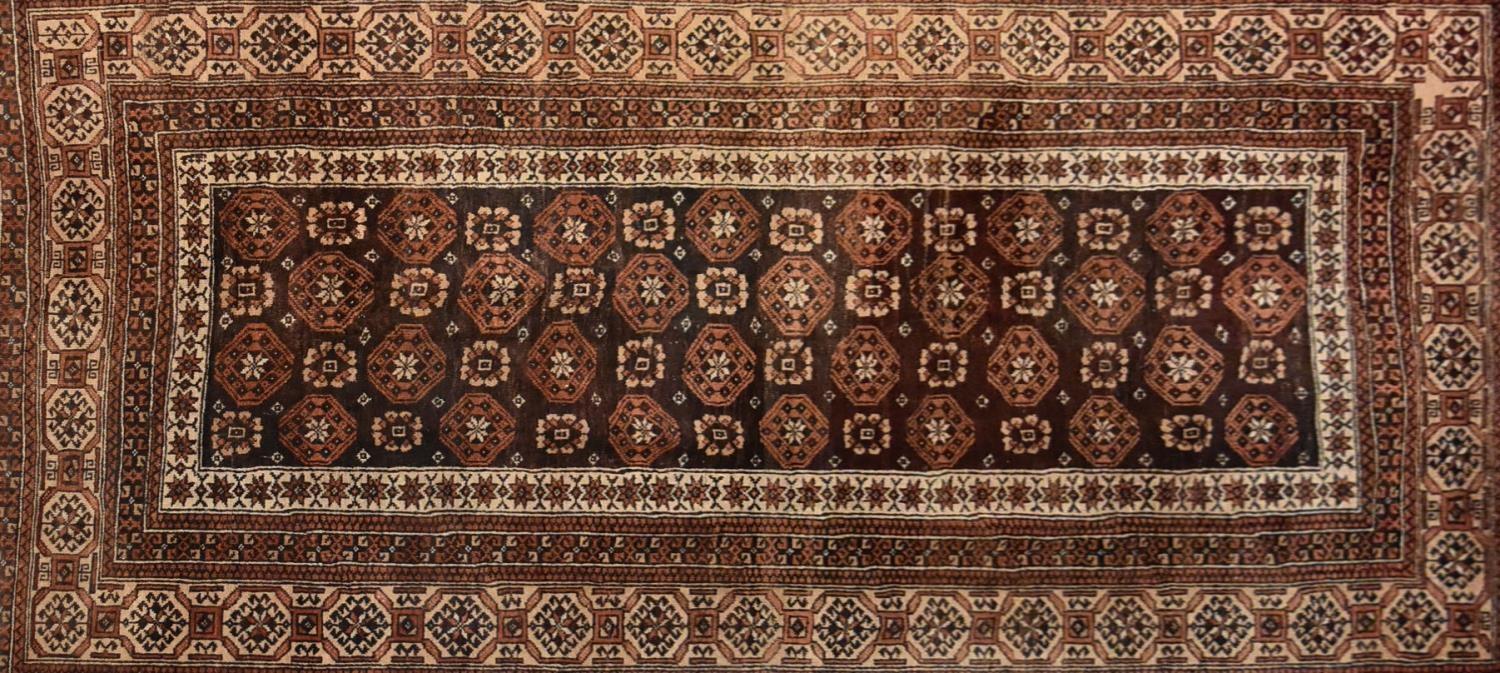 A Turkoman carpet with repeating gul moifs on a chocolate ground contained within stylised floral - Image 2 of 3