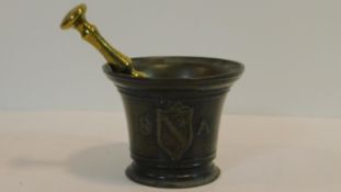 An antique bronze handled mortar and brass pestle. The handle has a textured design and the front of