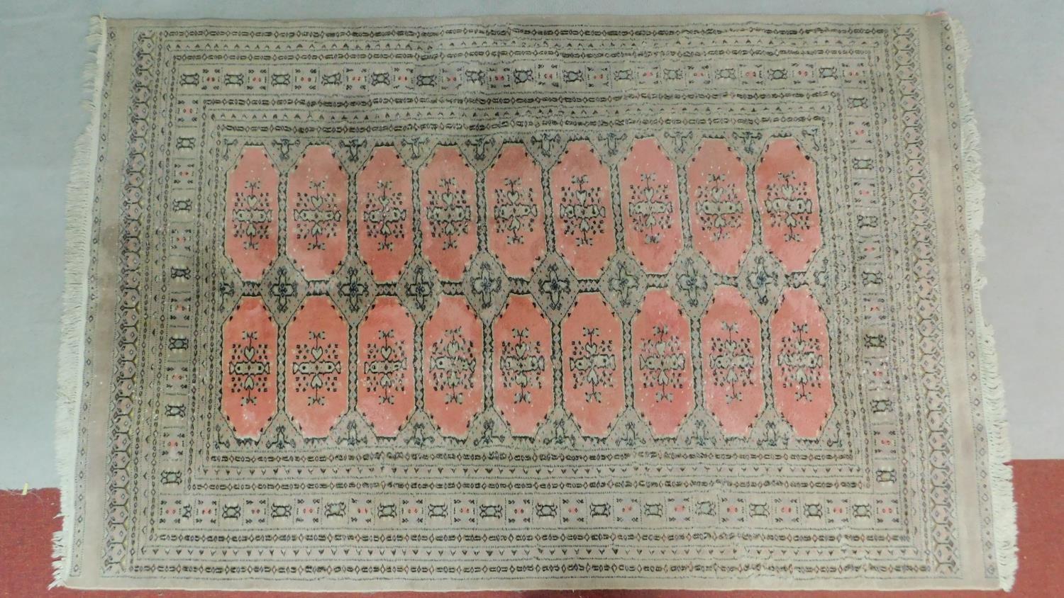 A woollen Bokhara style carpet with repeating lozenge motifs on rouge ground contained within