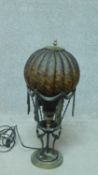 A metal table lamp in the form of an early hot air balloon supported by mythical winged figures. H.