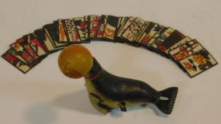 A vintage wind up tin plate toy of a seal with a ball on its nose that spins along with a set of