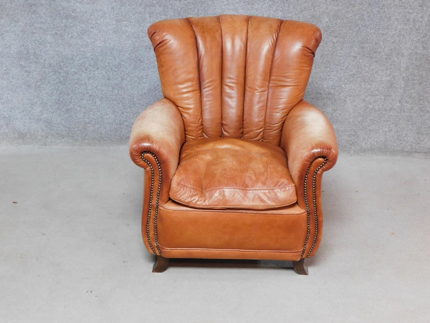 A contemporary Art Deco style armchair in tan leather with roll arms and a scallop shaped back H.