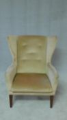 A mid century vintage wing back armchair on stained beech supports. H.87cm