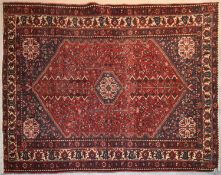 A Persian rug with central lozenge medallion with spandrels and gul motifs on a rouge field