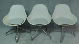 A set of three contemporary moulded tub chairs with squab cushions on quadruped chromium supports.