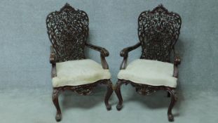 A pair of Burmese teak open armchairs with intricately carved scrolling foliate backs in floral