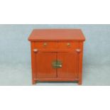 A red lacquered Chinese side cabinet with two frieze drawers above panel doors on block feet. H.74