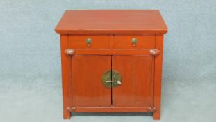 A red lacquered Chinese side cabinet with two frieze drawers above panel doors on block feet. H.74