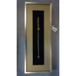 A framed and glazed Tibetan brass tantric staff (khatvanga), the handle with three faces and