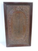 A 19th century framed Islamic repoussé copper plaque with calligraphy design and scrolling motif