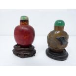Two Qing dynasty carved snuff bottles. One made from orange/red dappled realgar glass with a jade
