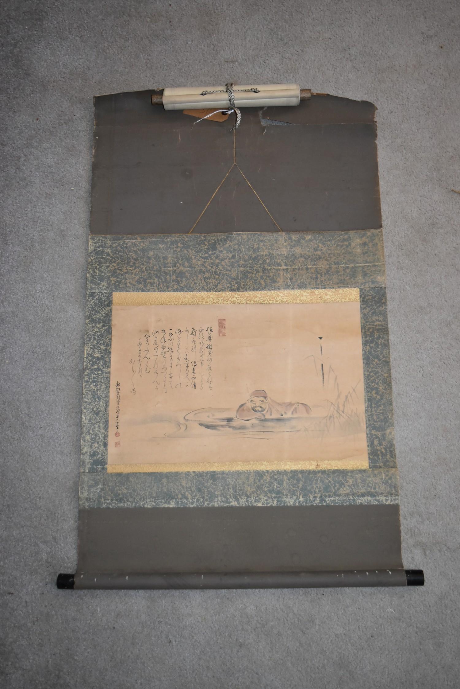 A Japanese mounted scroll, ink on paper, a man lying low in a punt in floral textile borders,