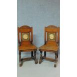 A pair of oak Arts and Crafts hall chairs with carved backs and solid seats on turned stretchered