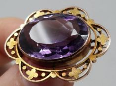 An antique pierced foliate design 9ct gold and amethyst oval brooch. Set to the centre with an