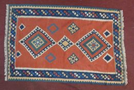 A Qashqai kelim rug with repeating diamond medallions on a terracotta field within geometric