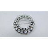 A white stone circular white metal brooch set with thirty eight round white paste stones in four
