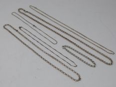 A collection of six silver chains. Including a heavy silver rolo link bracelet, and a white metal