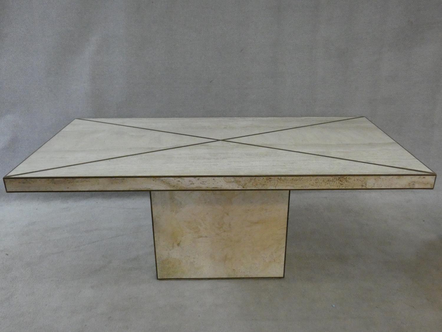 A brass bound travertine marble dining table on pedestal base. H.74xW.181xL.90cm