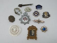 A collection of twelve antique brooches and badges. Including a carved mother of pearl brooch with