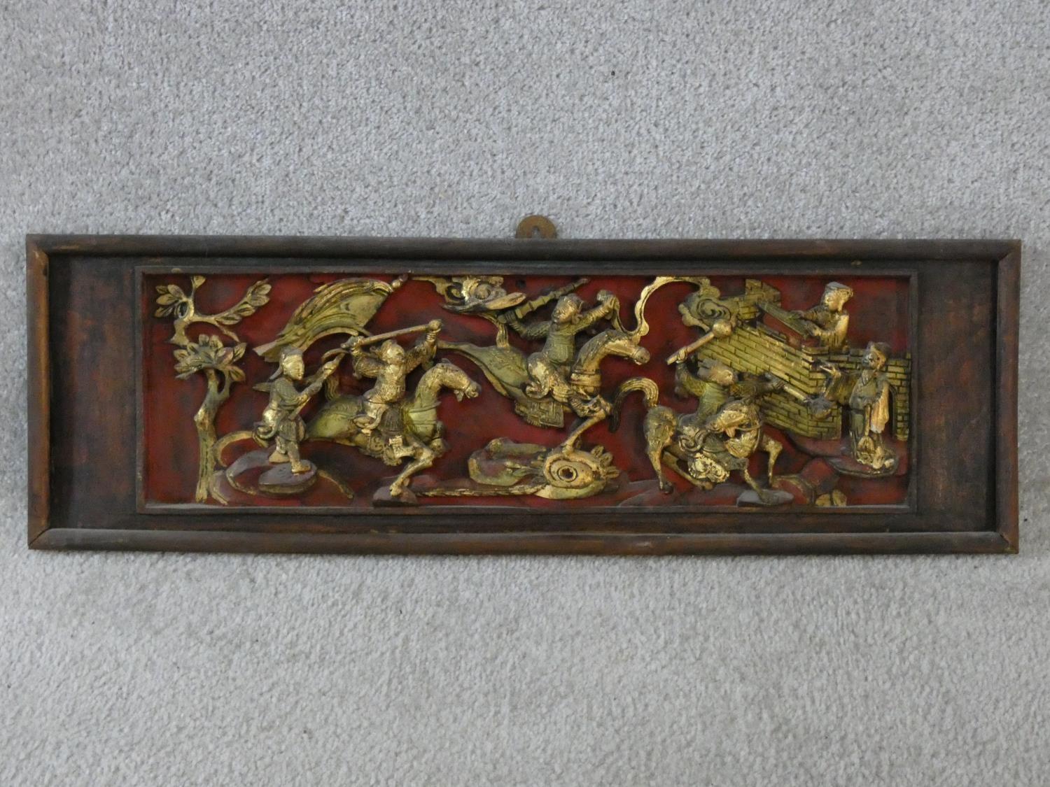 An antique Chinese carved lacquered and gilded panel with red round and warriors on horseback