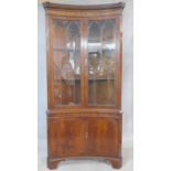 A Georgian style flame mahogany corner cupboard of concave outline with astragal glazed section