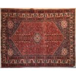 A Persian rug with central lozenge medallion with spandrels and gul motifs on a rouge field