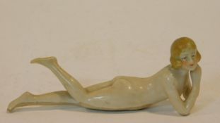 An antique hand painted porcelain figure of a nude lady lying with her leg up, mark to base and