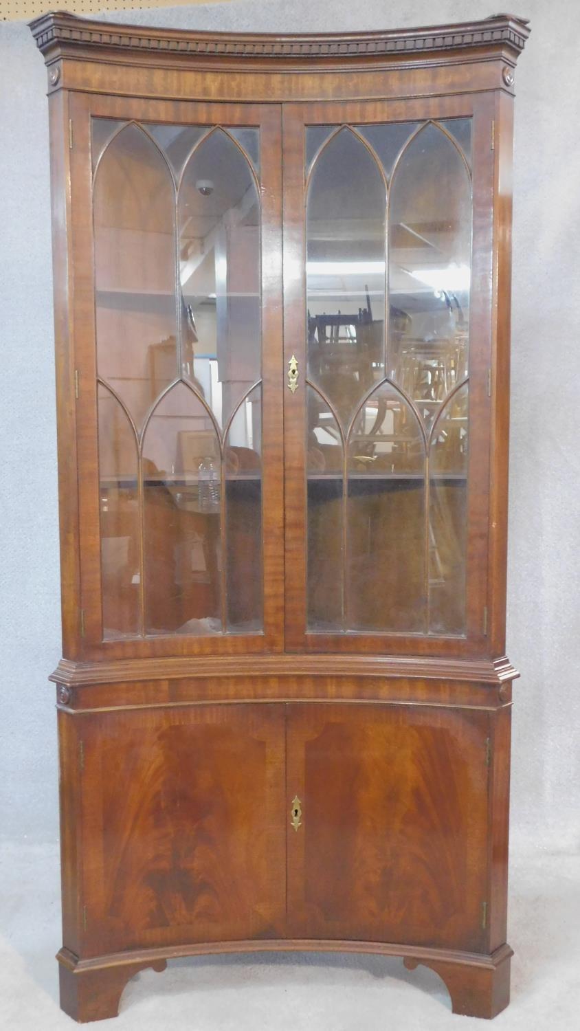 A Georgian style flame mahogany corner cupboard of concave outline with astragal glazed section